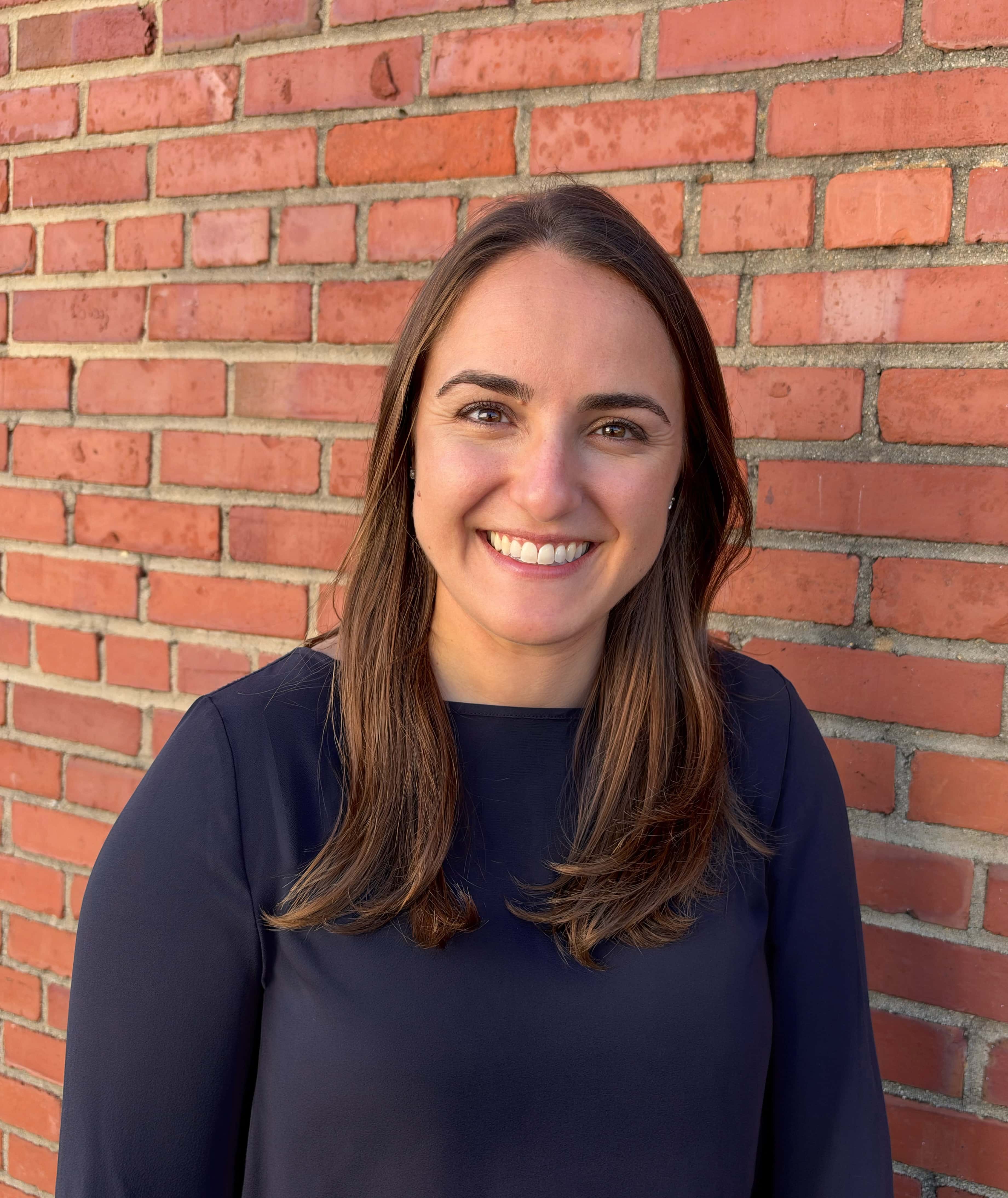 Woman with brown hair and a blue shirt standing in front of a brick wall