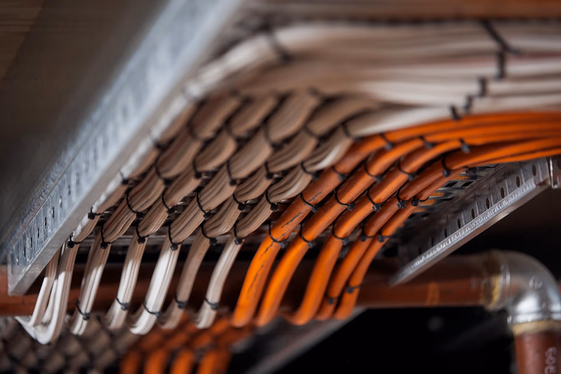 Neatly organized white and orange electrical cables secured with zip ties on a metal cable tray.