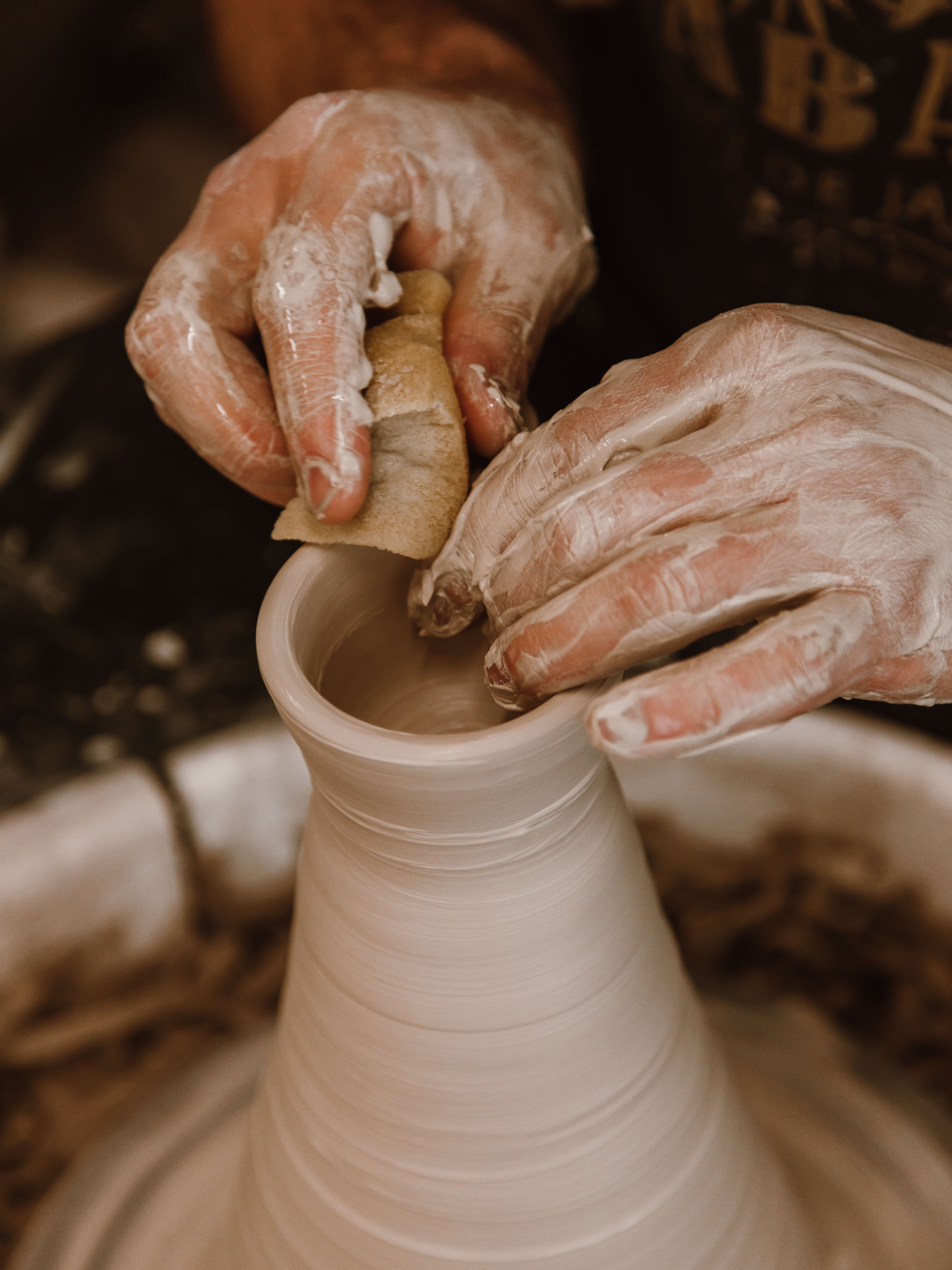 Mains couvertes d'argile façonnant un vase tournant sur un tour de potier.