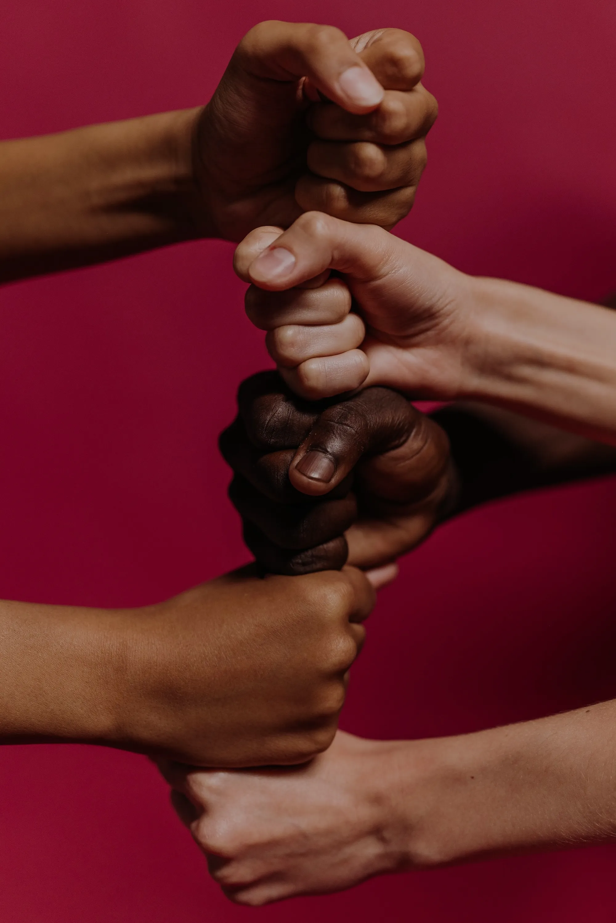 Poings fermés de différentes couleurs de peau empilés en signe d'unité sur fond rouge.
