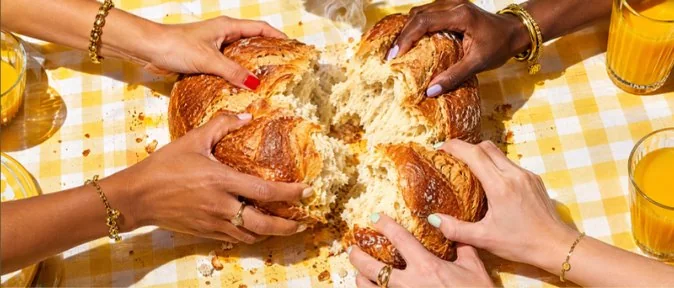 Hands tearing a loaf at a gingham table