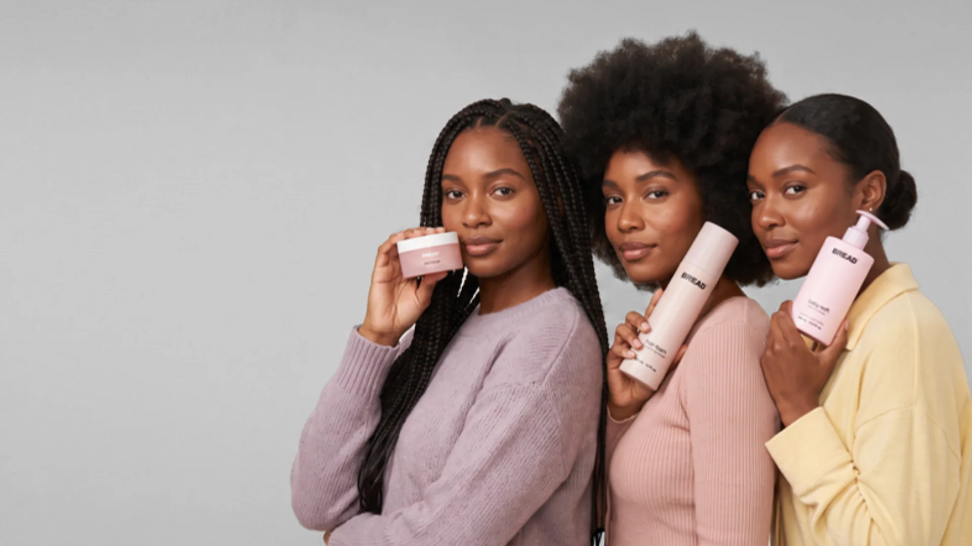 Three women holding BREAD haircare products
