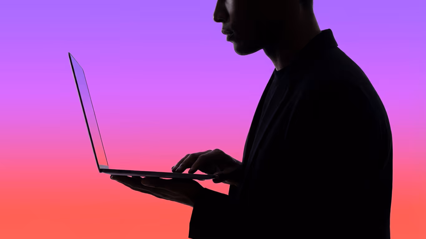 Silhouette of a person typing on a laptop against a gradient background of purple to red.
