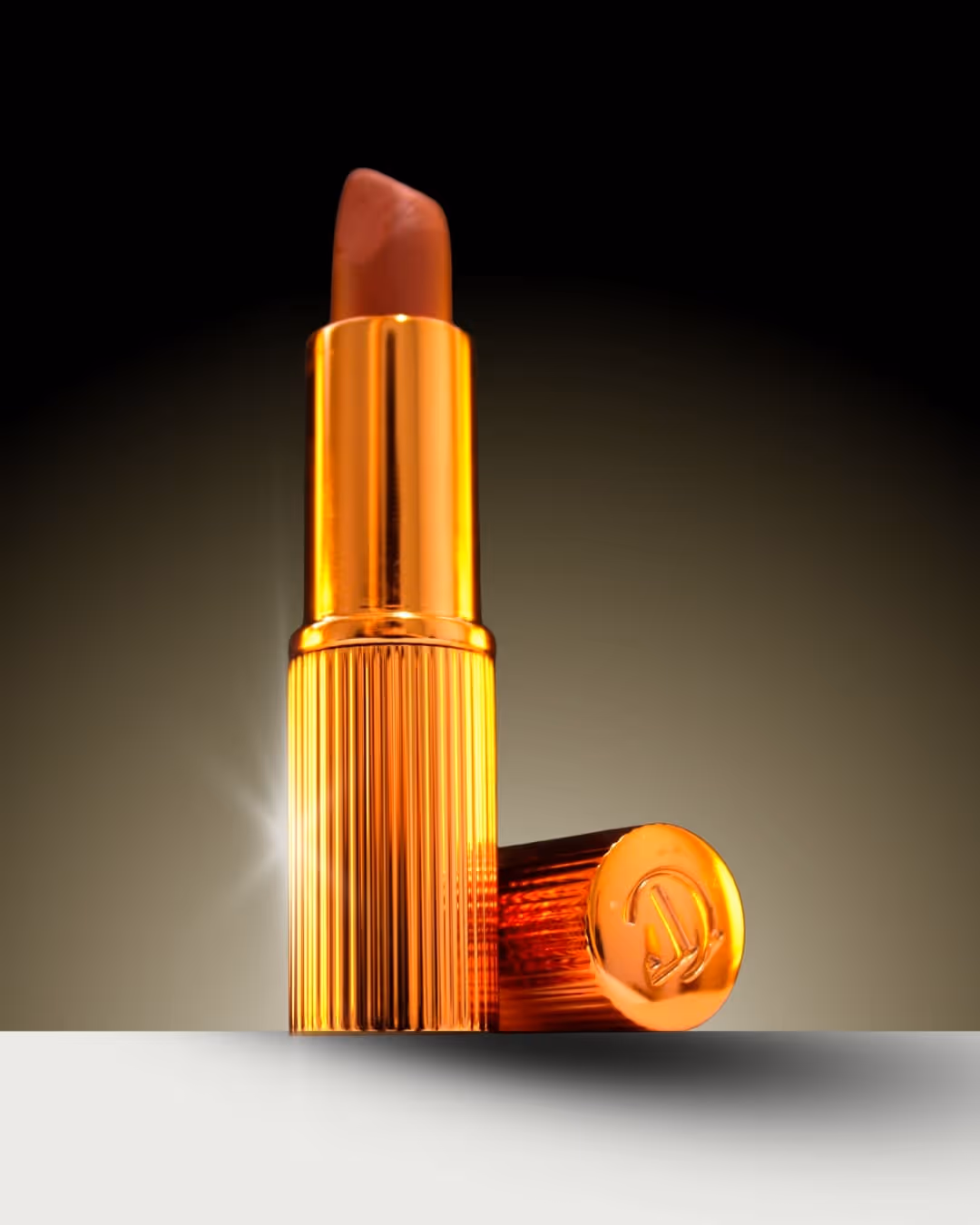 Close-up of an open brown lipstick with a shiny gold ribbed case and cap resting beside it.
