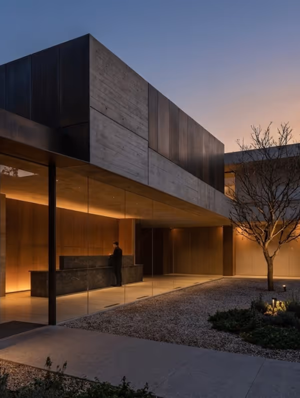 Modern building at dusk with large glass windows and a person standing at a dark stone reception desk inside.