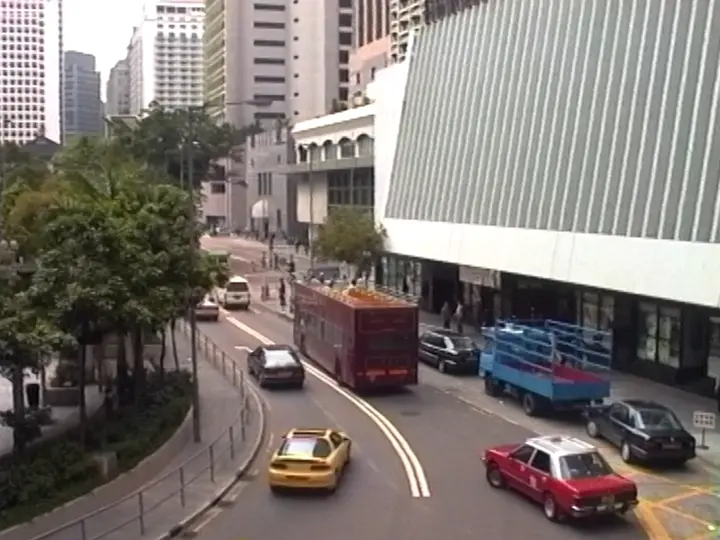 Urban street scene with several cars, a red double-decker bus, and a blue utility vehicle near tall buildings.