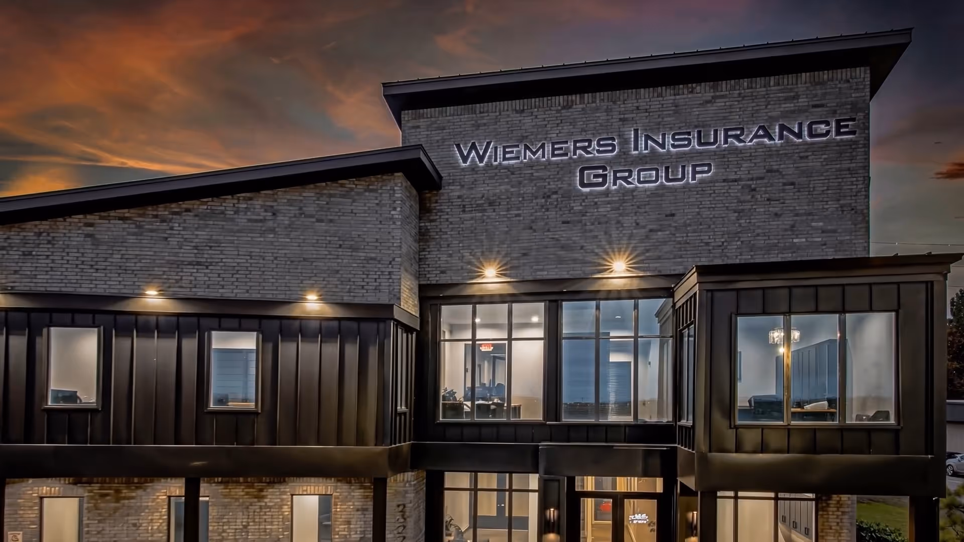 Modern brick and metal office building of Wiemers Insurance Group illuminated at dusk.