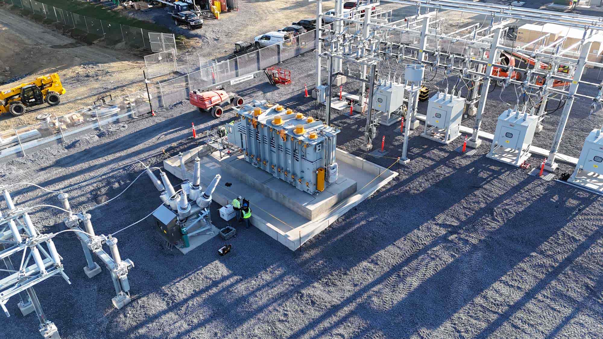 Aerial view of an electrical substation with transformers, power lines, and workers in safety gear.