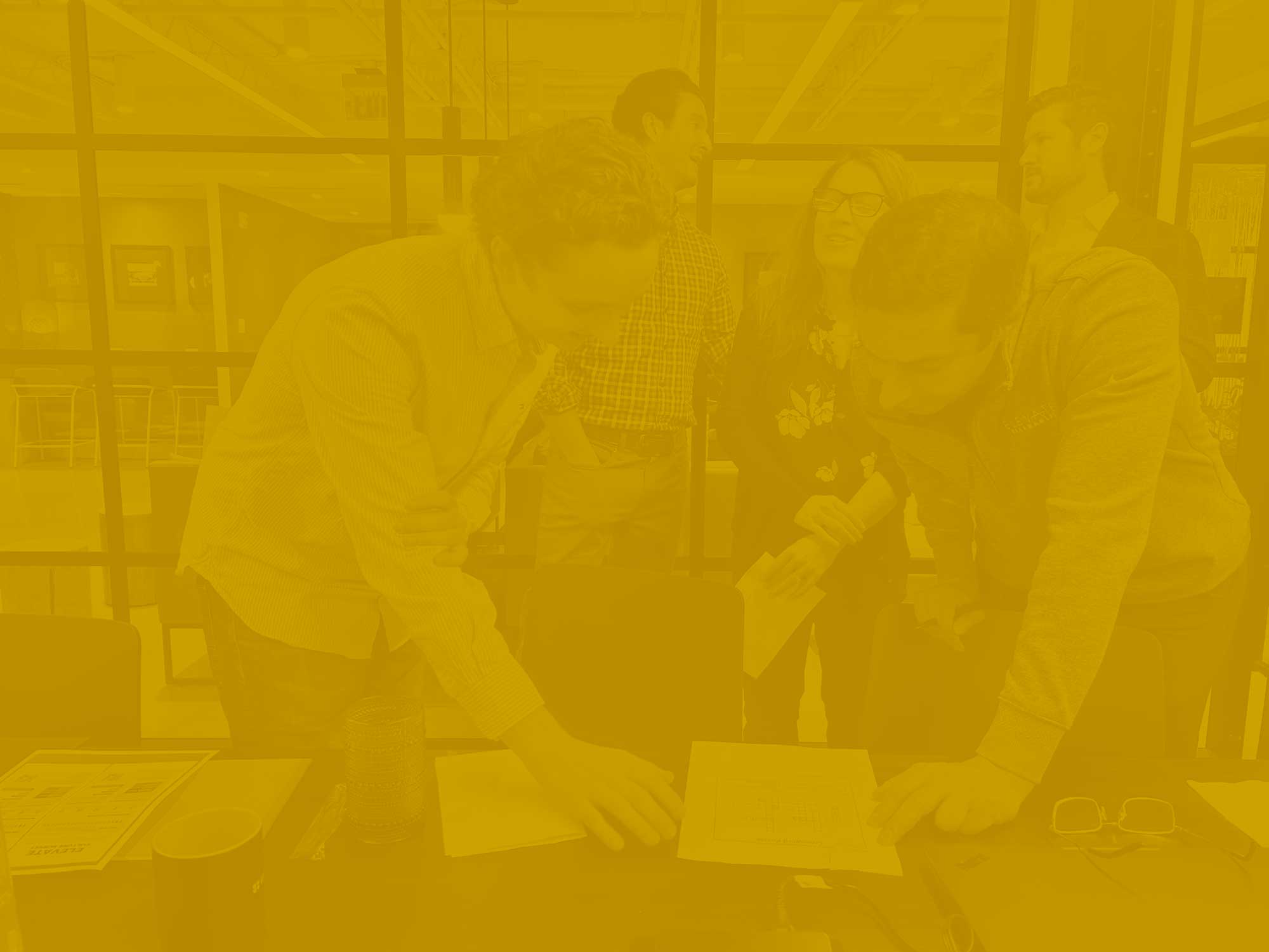 Yellow-gold tonal photo of professionals leaned together over paperwork.