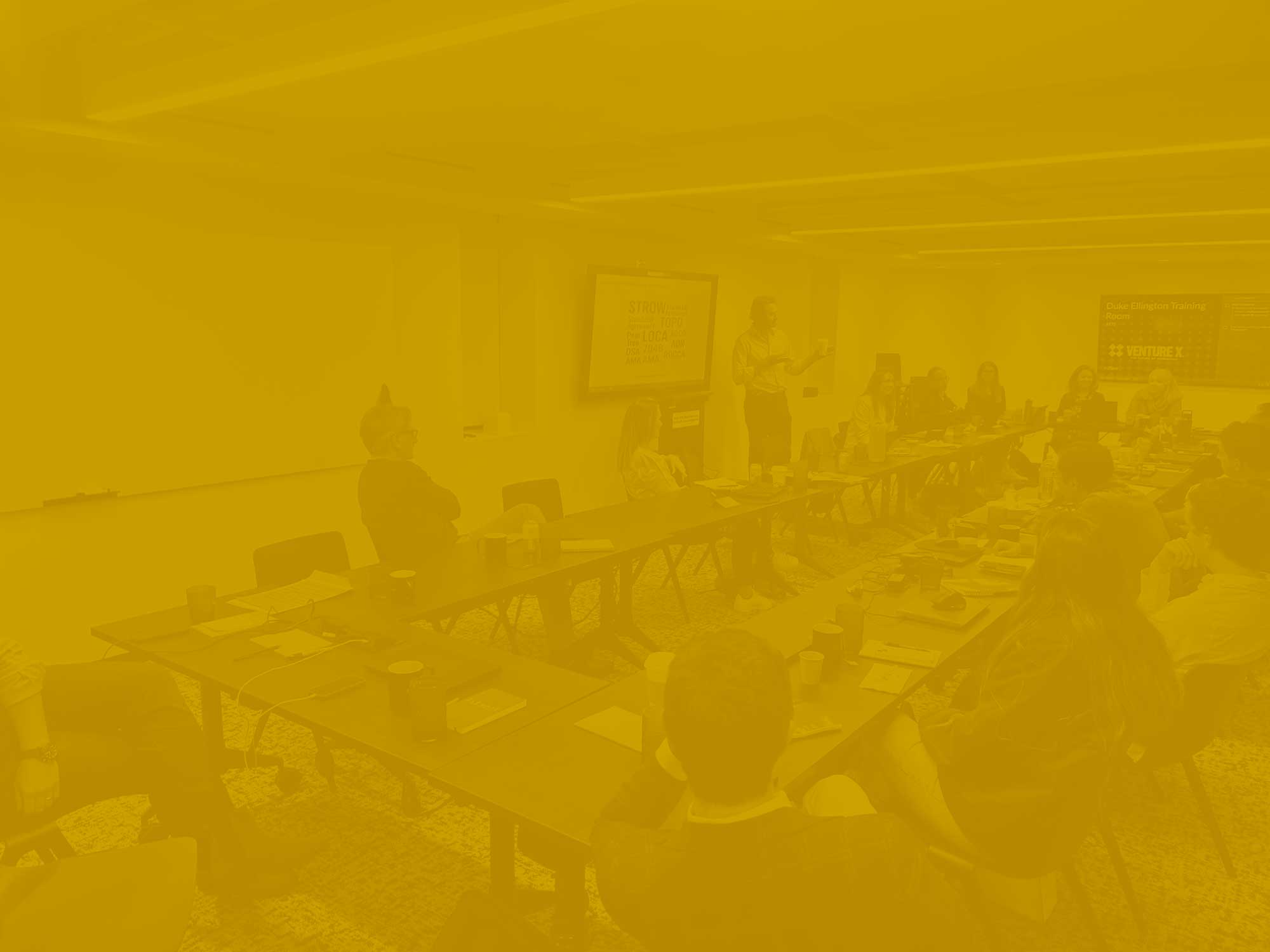 Yellow-gold tonal photo of a large team in a conference room.