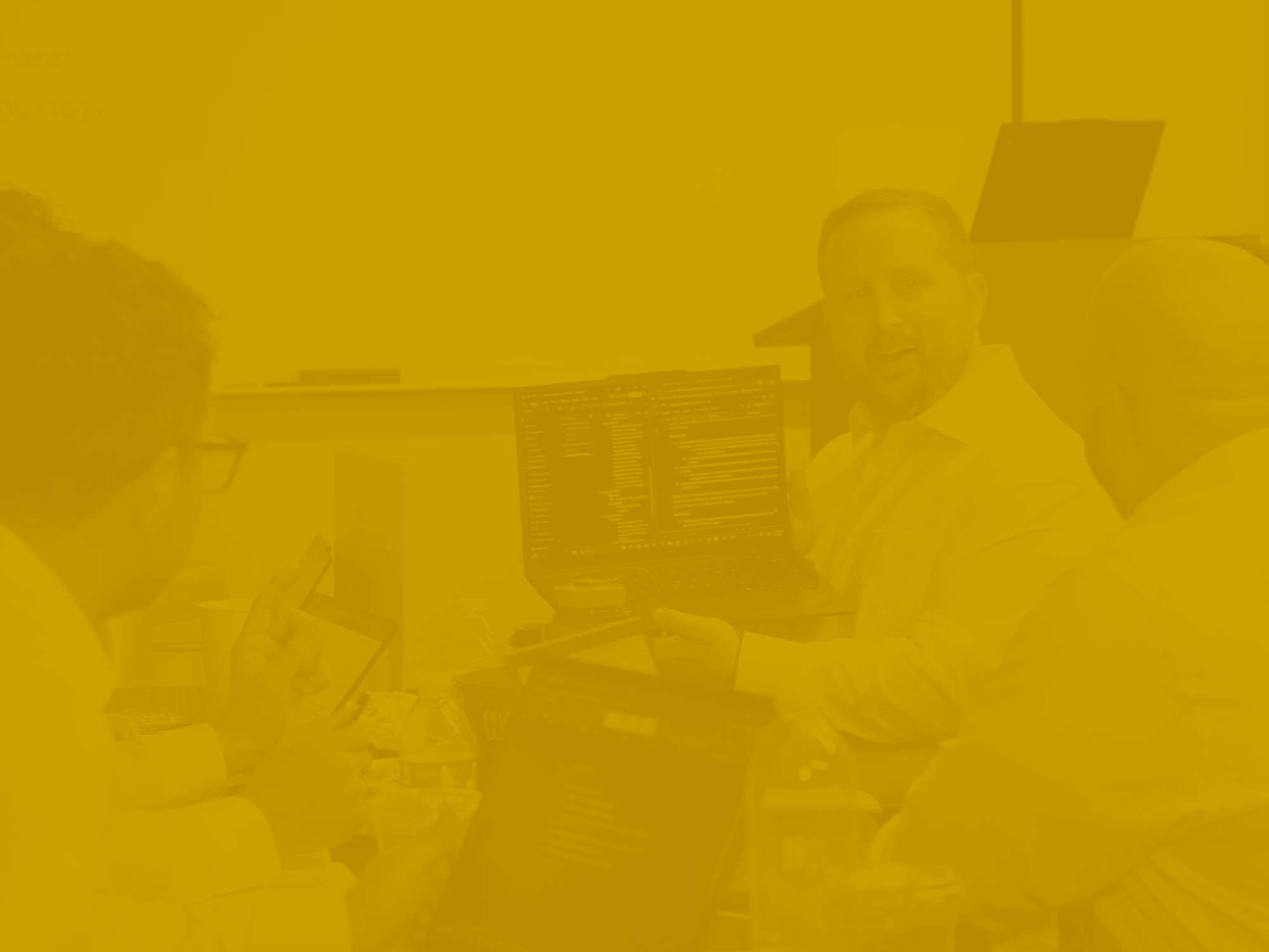 Yellow-gold tonal photo of a man sharing a laptop monitor with colleagues.