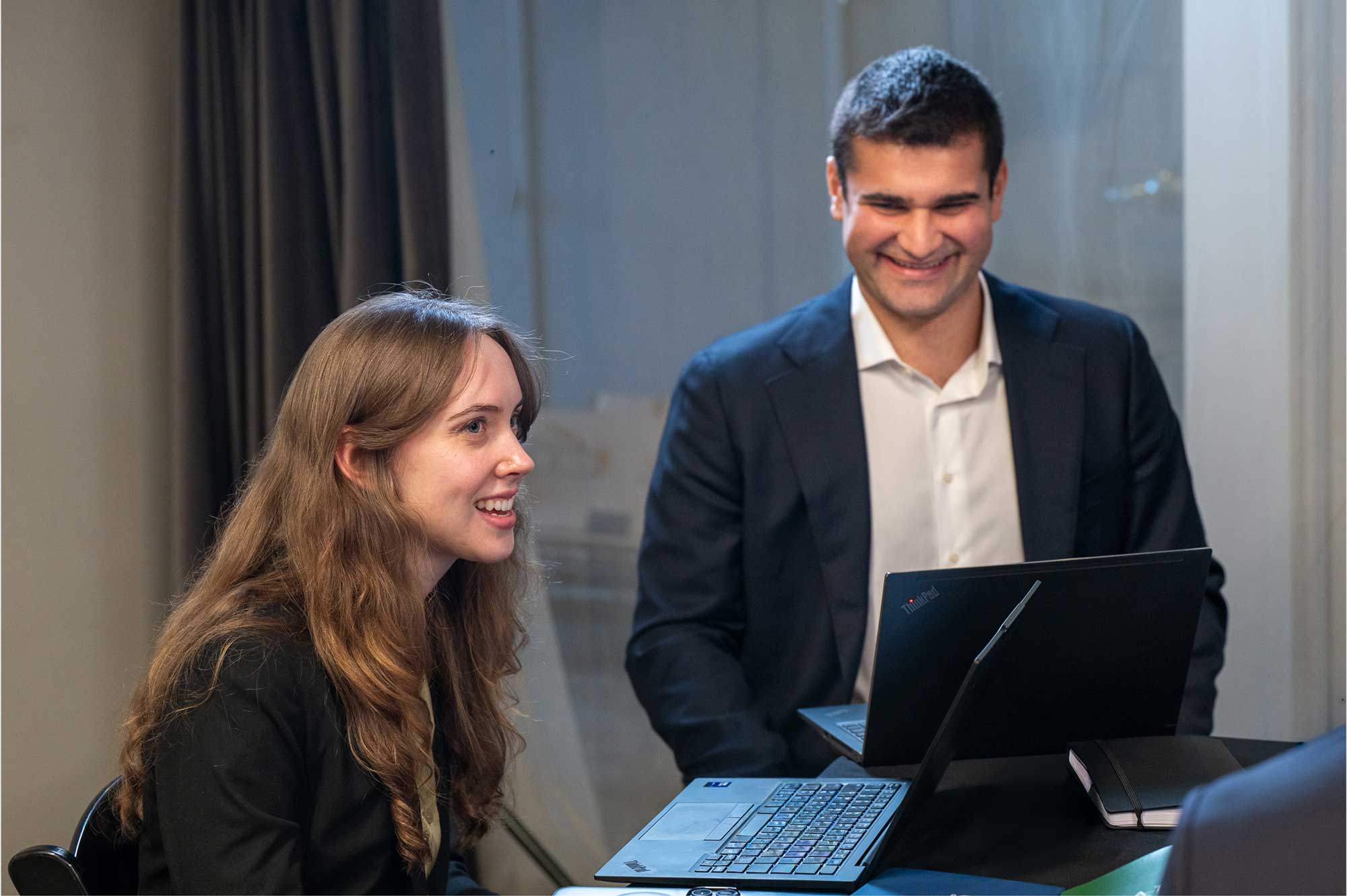 Two business professionals smiling and working together on laptops at a table.