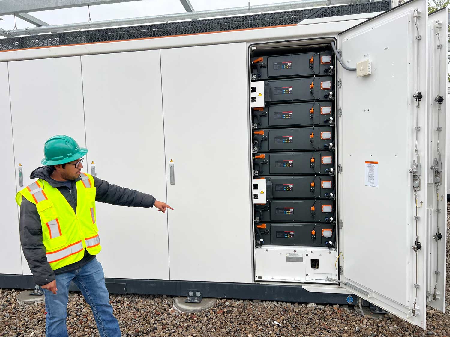 Construction workers operating a crane to lift a large electrical container in a power substation.
