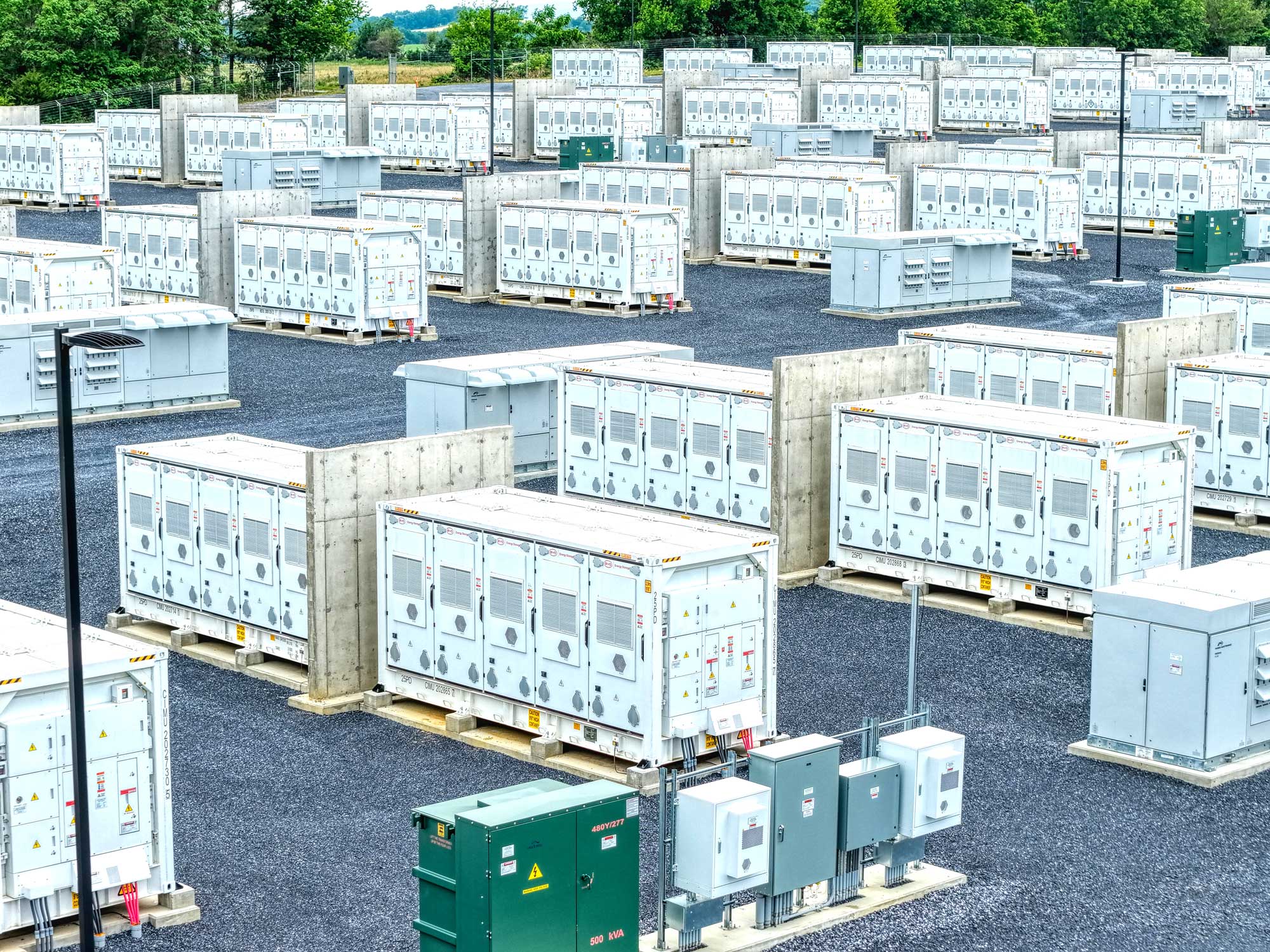 Aerial view of an electrical substation with transformers, power lines, and workers in safety gear.