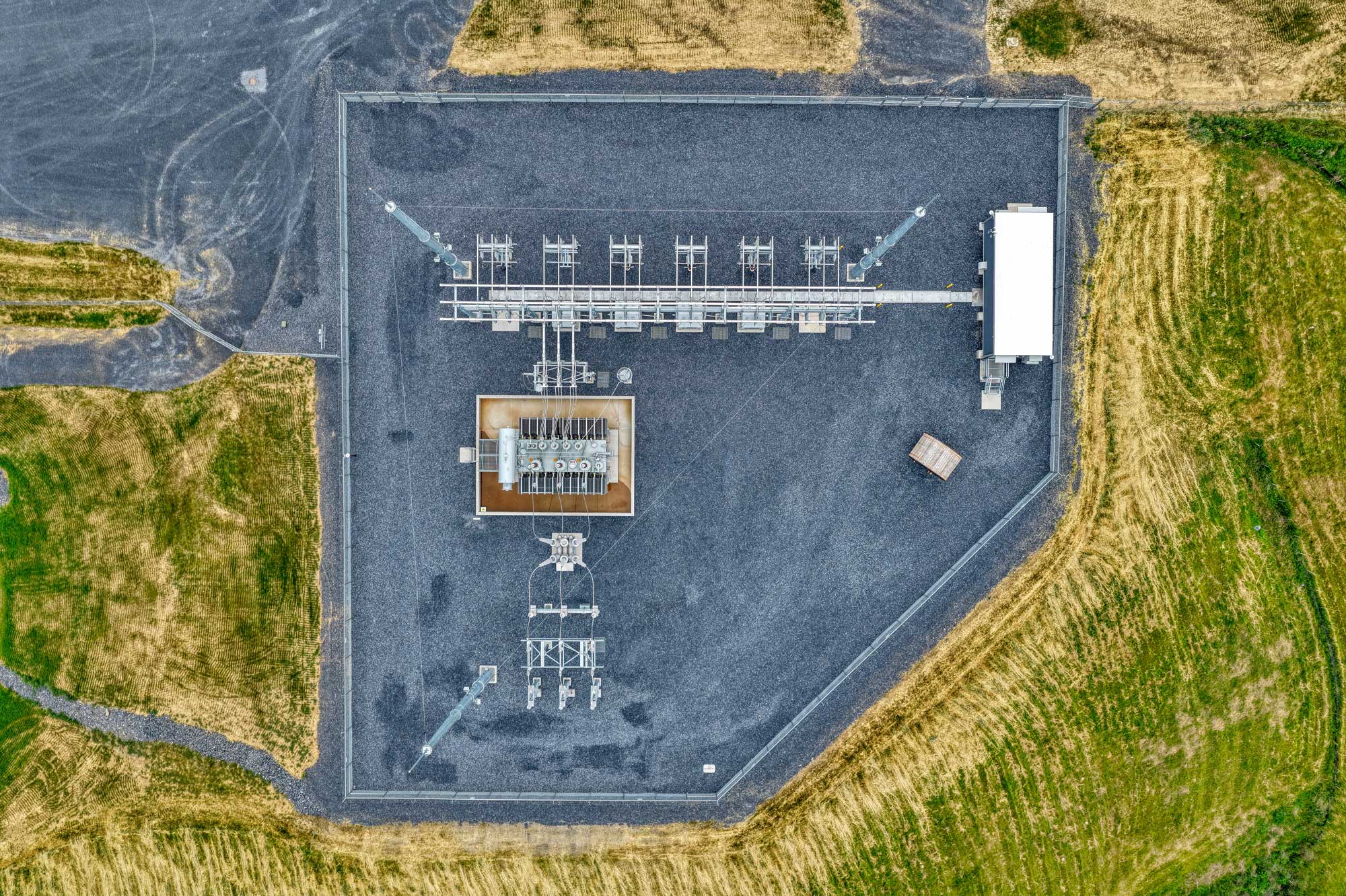 Construction workers operating a crane to lift a large electrical container in a power substation.