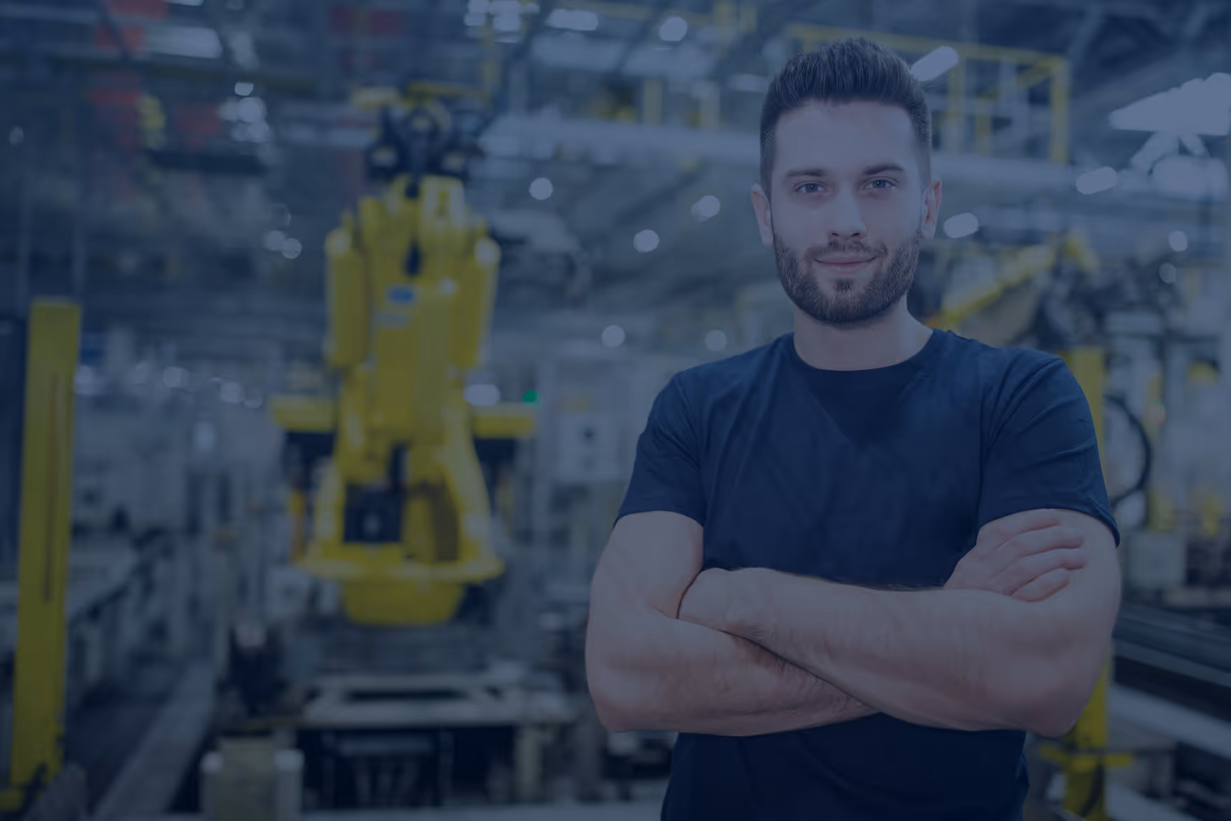 Confident man with folded arms standing in a modern factory with industrial machinery in the background.