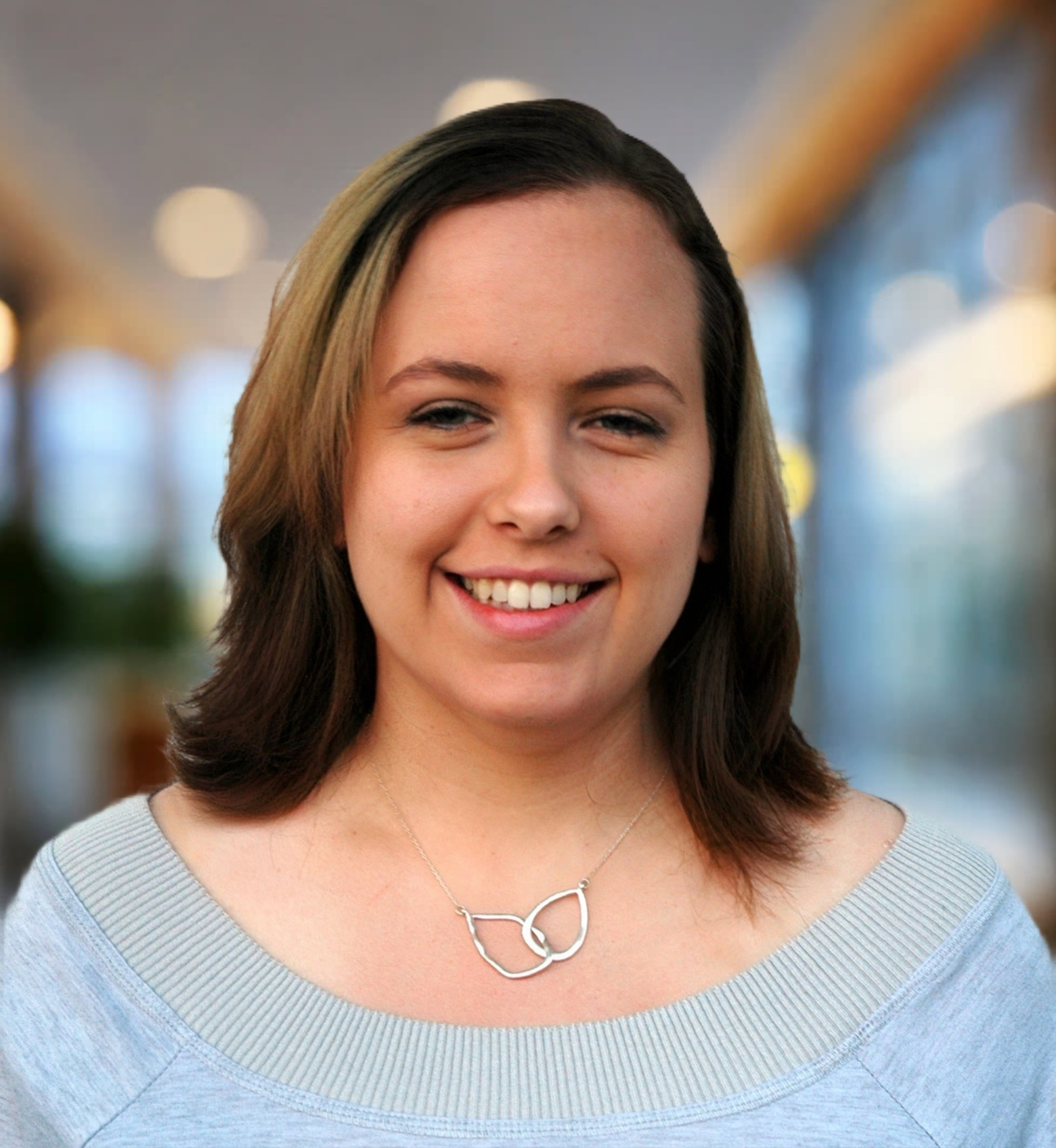 Smiling woman with shoulder-length hair wearing a gray top and a silver leaf-shaped necklace.