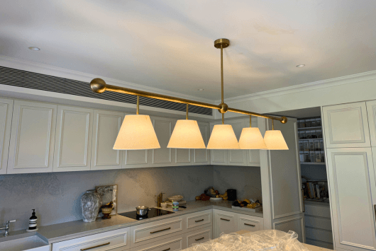 Modern kitchen with white cabinets and a brass linear chandelier with six lampshades hanging above the counter.