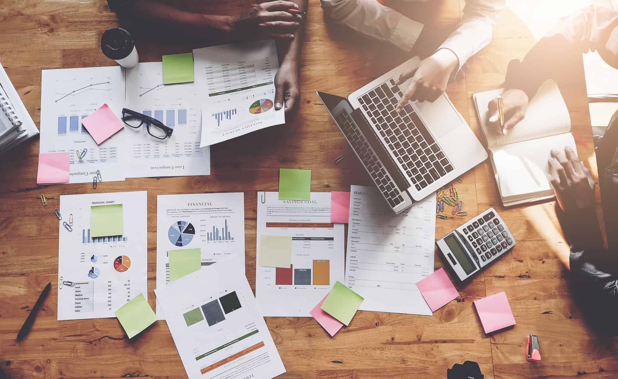 paper scattered on table with people working around it