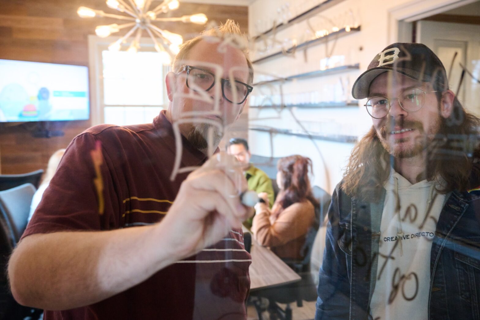 Two men writing on a glass wall at a full-service agency