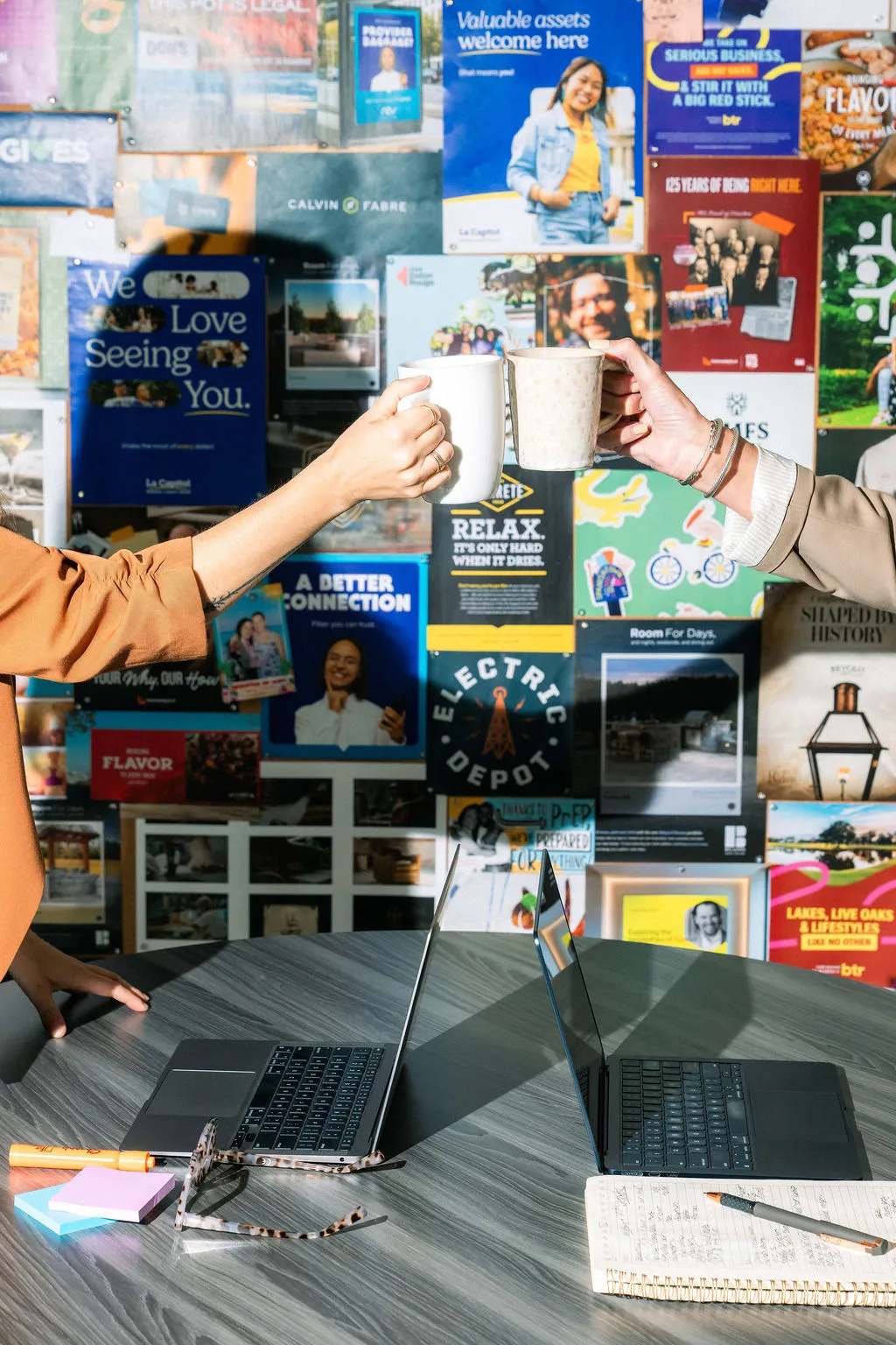 Two team members toasting coffee mugs with laptops on a table