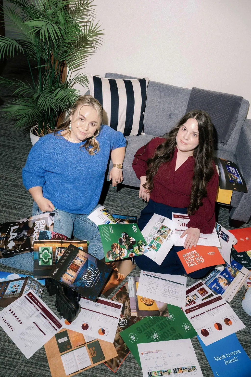Two women sitting on the floor with piles of agency work scattered around