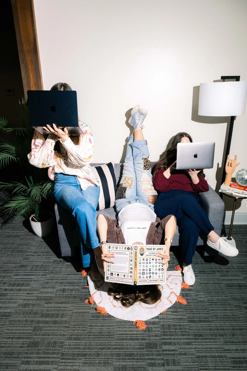Three team members lounging on a couch holding laptops in front of their faces