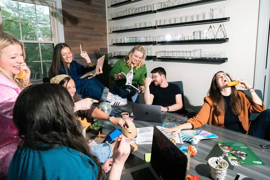 Team members laughing around a table, several holding bananas to their ears like phones