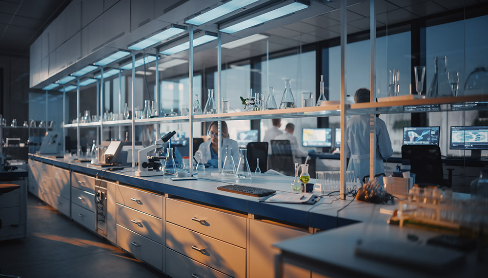 Modern biomedical research lab with glassware, microscopes, and scientists working at computer stations.