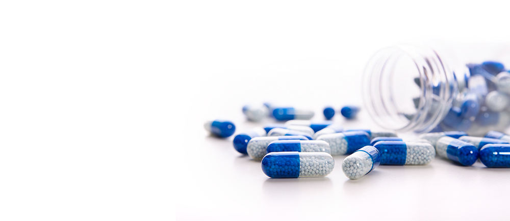 Blue and white capsules spilling out from a transparent container on a white surface.