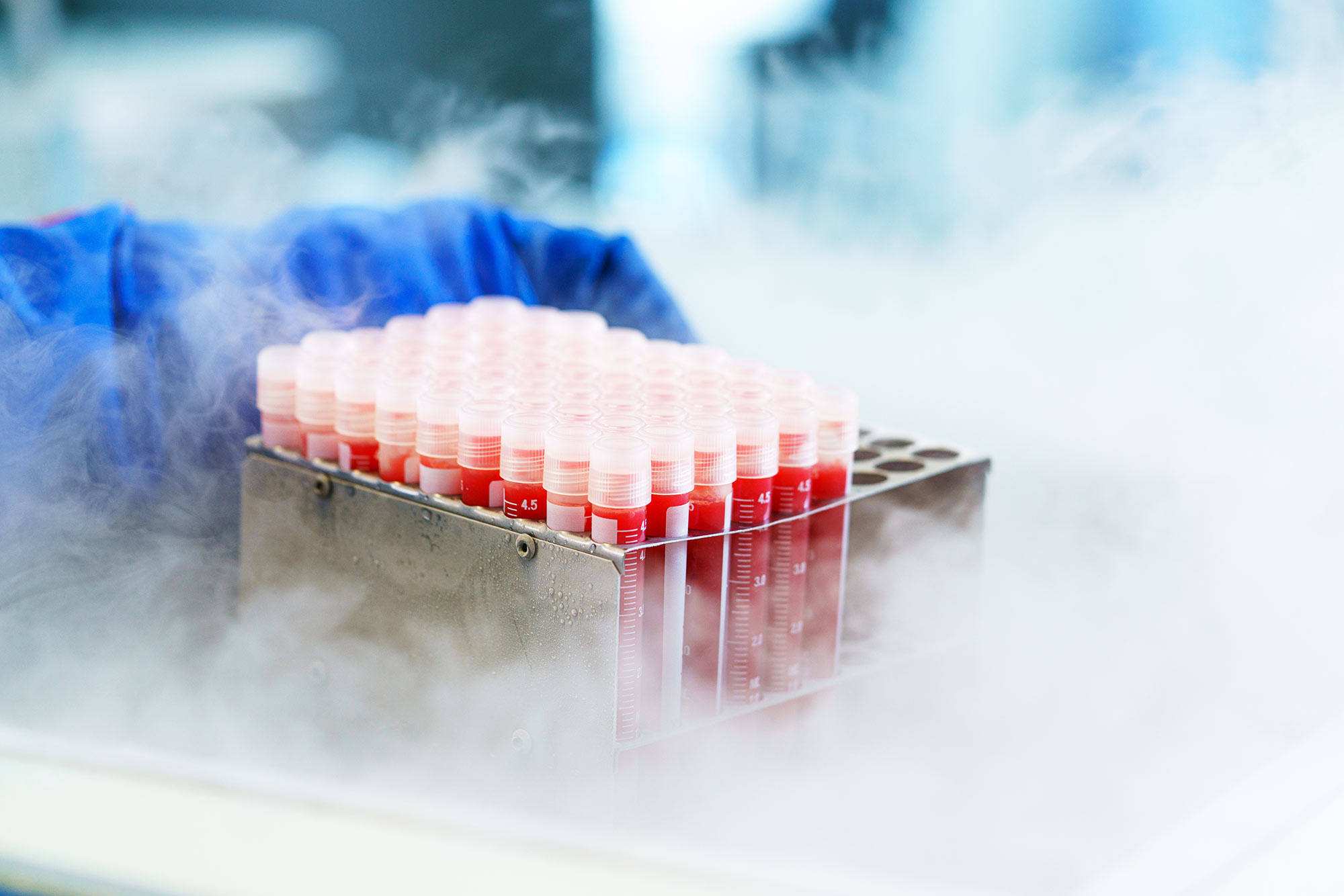 Rows of capped blood sample vials in a metal rack surrounded by laboratory mist or vapor.