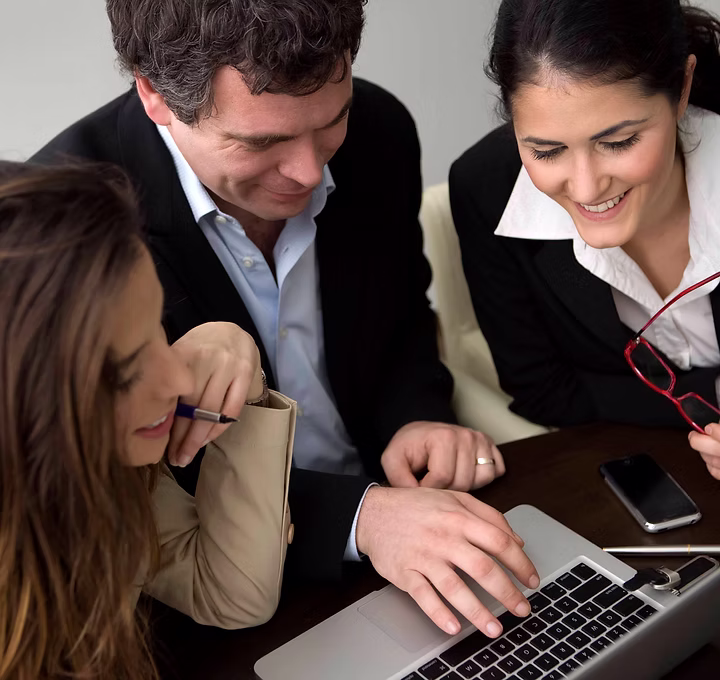 Three business people smiling and looking at a laptop screen during a consultation.