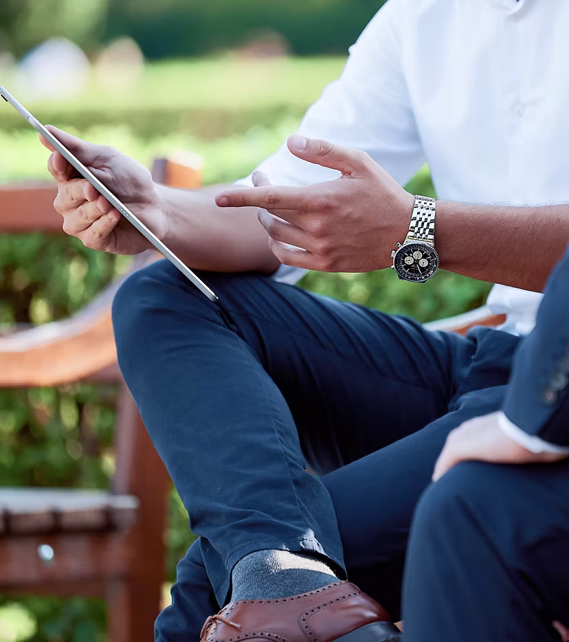 Man in business casual attire holding a tablet, gesturing with his hand during a conversation outdoors.