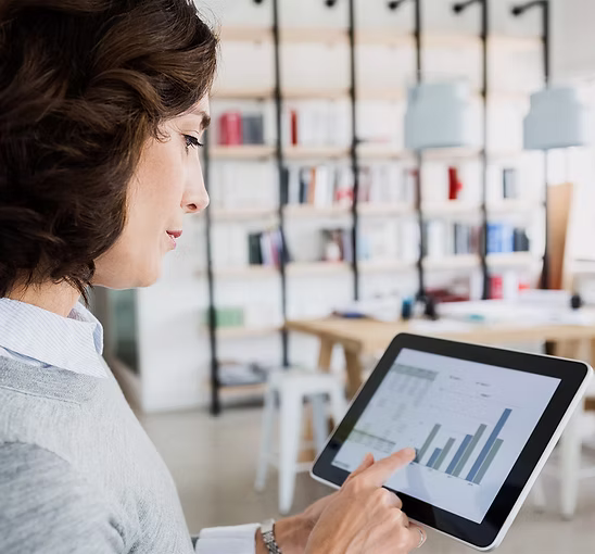 Woman using a tablet showing bar charts and graphs in a modern office space.