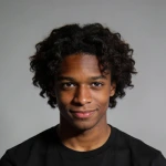 Smiling young man with curly hair wearing a black shirt against a gray background.