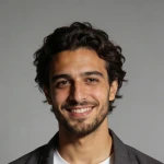 Portrait of a smiling young man with curly dark hair wearing a dark jacket over a white shirt