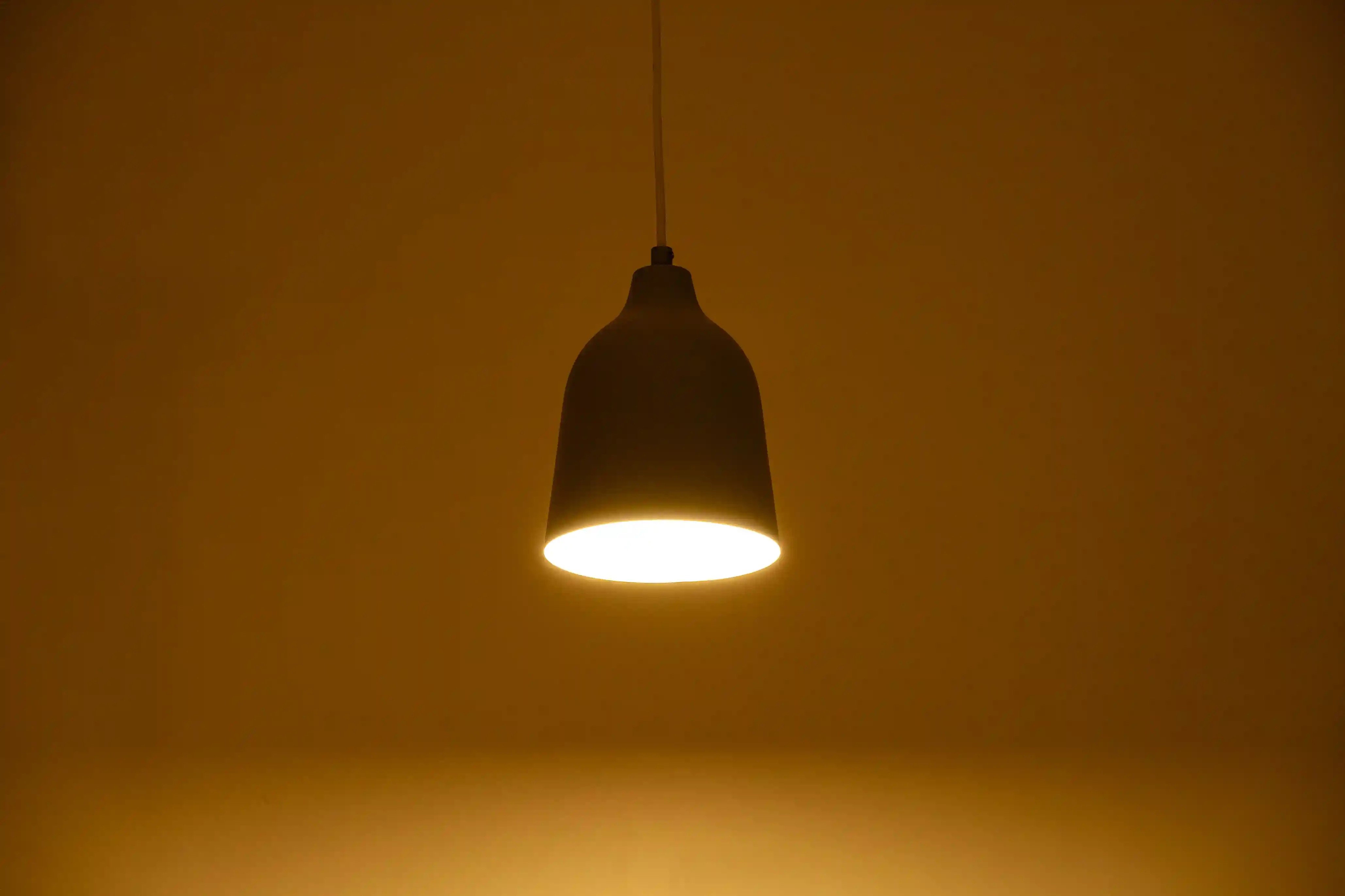 A single pendant lamp with a dark shade hanging and glowing warmly in a dim space.
