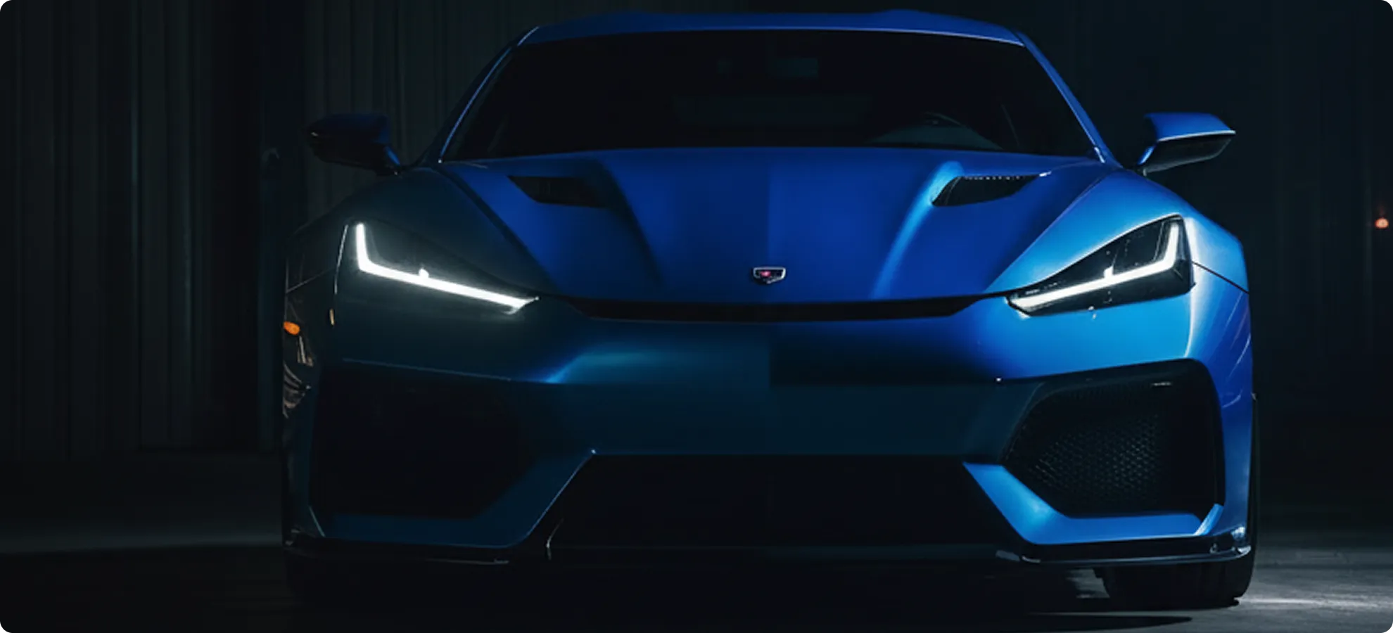 Front view of a blue sports car with LED headlights illuminated in a dark setting.