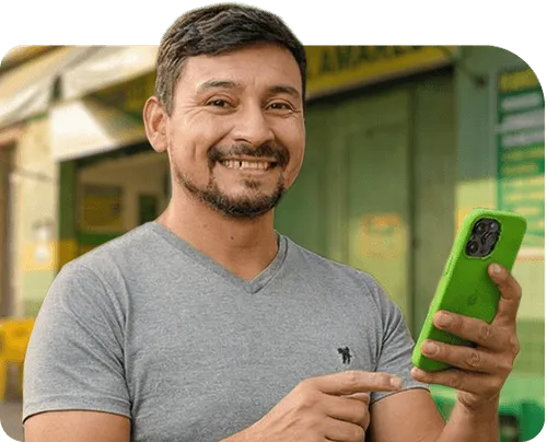 Smiling man pointing at a green smartphone in an outdoor urban setting.