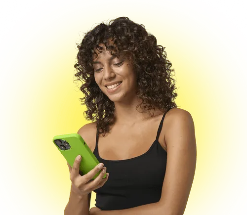 Smiling woman with curly hair in black tank top looking at her green smartphone against yellow background.