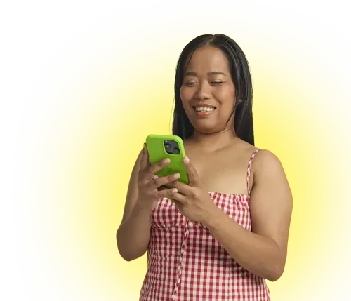 Smiling woman wearing red checkered dress looking at her green smartphone against yellow background.