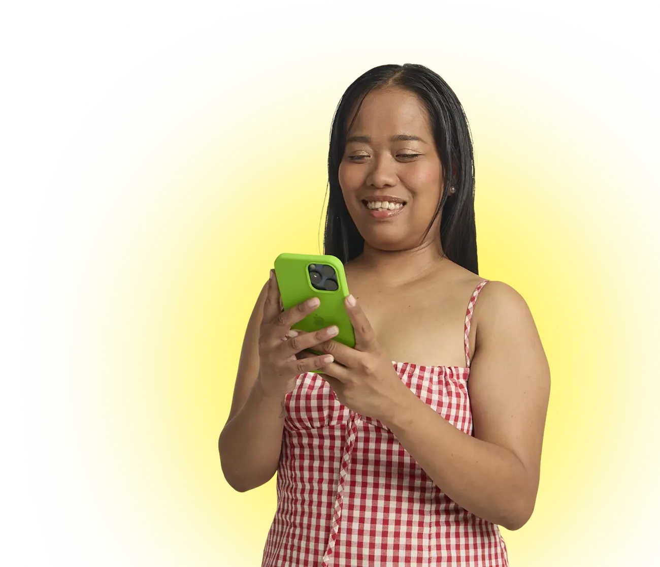 Smiling woman wearing red checkered dress looking at her green smartphone against yellow background.
