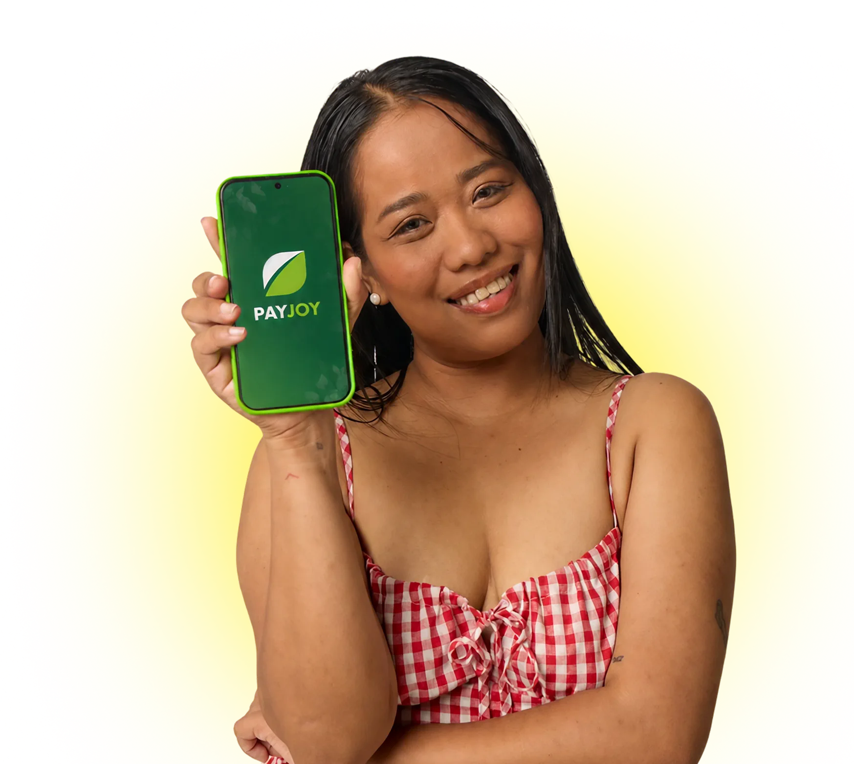 Smiling woman in red checkered top holding phone displaying PayJoy app logo on green screen.