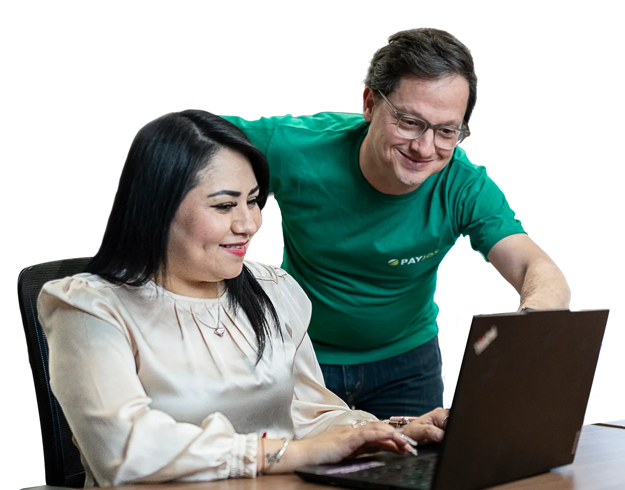 Smiling man in green shirt helps woman using a laptop at a desk.