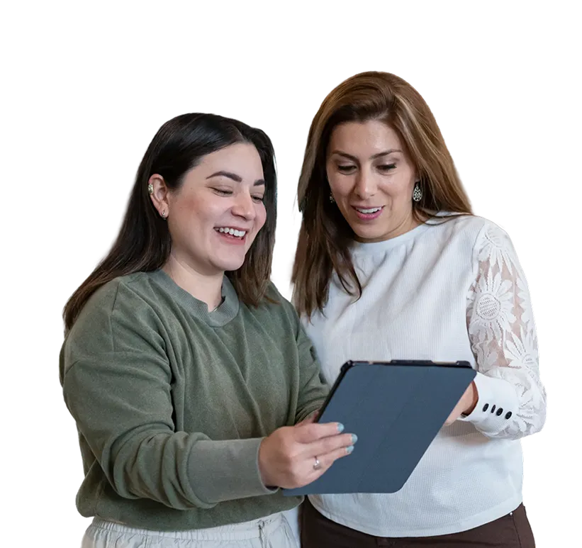 Two women smiling and looking at a tablet device together.