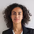 Portrait of a woman with curly hair wearing a black blazer and white shirt against a white background.