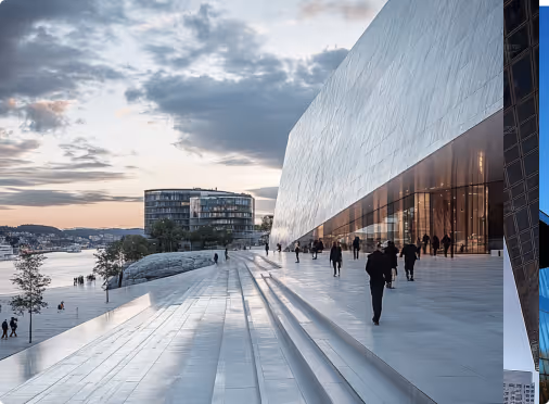 Modern waterfront building with large white angular facade and wide steps, people walking near the entrance at dusk.