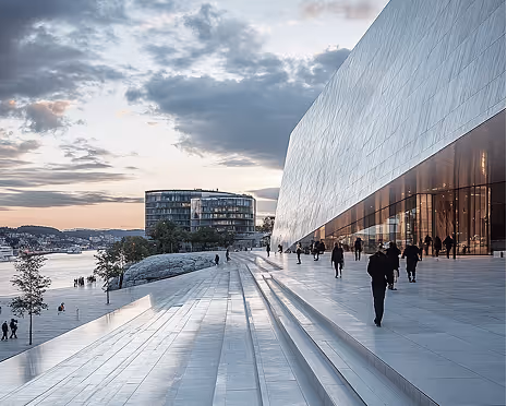 People walking on large, modern stone steps beside a reflective glass building under a cloudy sky at sunset.