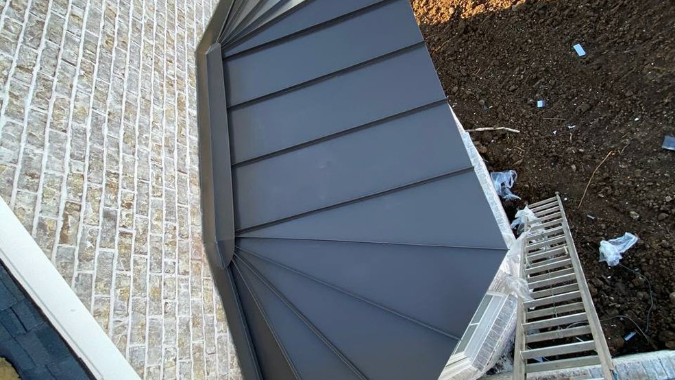 Gray standing seam metal roof formed around a dormer