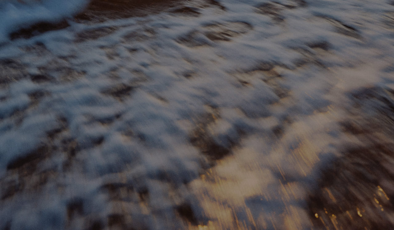Blurred close-up of water surface with light reflections in blue and gold tones.